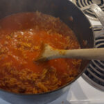 Tomato Bolognese cooking in a black pot on a stove with a wooden spoon