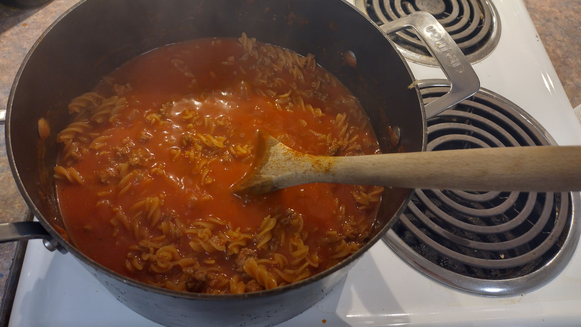 Tomato Bolognese cooking in a black pot on a stove with a wooden spoon