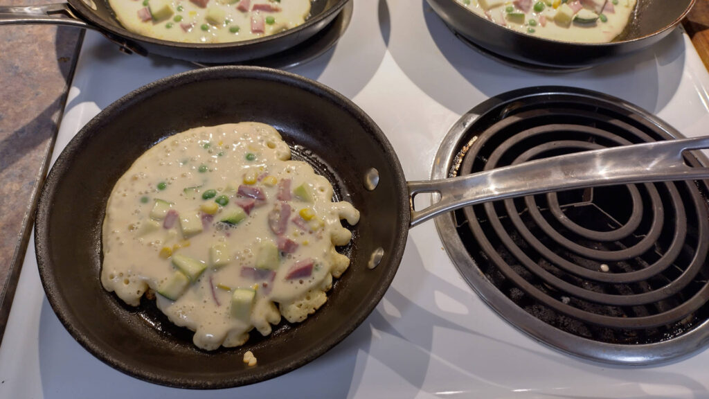 Corned beef fritters cooking on three frying pans